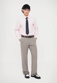 Lichtroze overhemd, marineblauwe stropdas met witte stippen, grijze broek met patroon, bruine riem en zwarte schoenen met witte accenten.