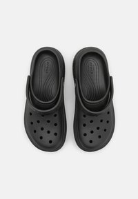 Sabots en caoutchouc noir avec un design perforé, une sangle à l'arrière et une semelle intérieure texturée pour le confort, présentant une finition extérieure lisse.