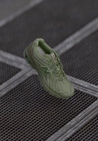 Baskets de sport vertes avec une tige texturée, un design à lacets et un logo "N" proéminent. Elles disposent d'un cushioning et d'une semelle en caoutchouc, adaptées à une utilisation active.