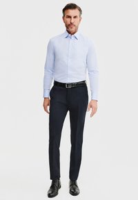 Jasnoniebieska, długosleeve koszula połączona z ciemnymi spodniami, czarnym paskiem i czarnymi butami na sylwetce mężczyzny na jednolitym tle.