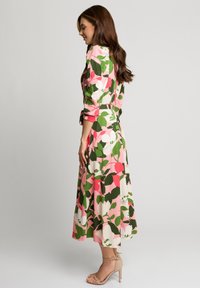 Kwiatowa sukienka midi w odcieniach różu, zieleni i bieli; lekki materiał; długie rękawy; taliowana; w połączeniu z beżowymi sandałkami na obcasie.