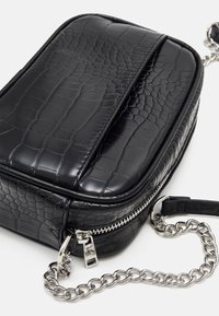 Czarna torba z ekologicznej skóry o fakturze przypominającej krokodyla, o prostokątnym kształcie, ze srebrnym łańcuszkowym paskiem i zamknięciem na zamek.