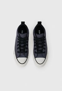 Par sportski sive platnene tenisice s crnim vezicama i bijelim gumennim vrhovima, gledano odozgo na bijeloj pozadini.