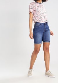 Camisa corta de manga corta con estampado floral en tonos rosados, combinada con pantalones cortos de mezclilla azul hasta la rodilla. Los pantalones cortos tienen una textura suave y un diseño estándar de cinco bolsillos.