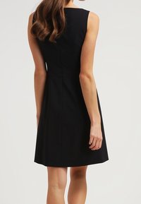 Vestido negro sin mangas con un corsé ajustado y falda acampanada. Tela suave, hasta la rodilla, con escote cuadrado y sin cierres visibles.