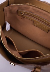 Interior de un bolso de mano de cuero marrón con forro de tela, un bolsillo con cremallera, dos compartimentos abiertos y una etiqueta de cuidado blanca visible.