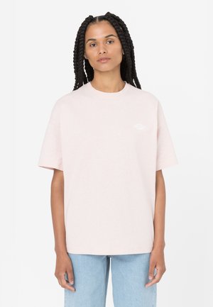 Camiseta de algodón rosa claro con mangas cortas, cuello redondo y un logo bordado en el lado izquierdo del pecho. Combinada con jeans azul claro.