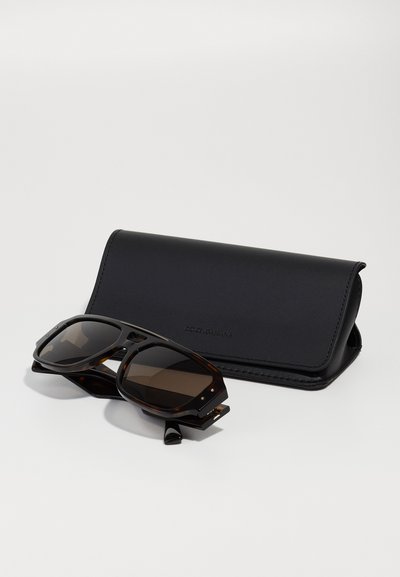 Sunglasses with a tortoiseshell frame and dark lenses, paired with a slim black leather case featuring a logo. Flat and rectangular design.