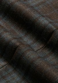 Tessuto a motivo houndstooth marrone con una superficie morbida e strutturata, caratterizzato da sfumature di blu e marrone scuro in un design tessile intrecciato.