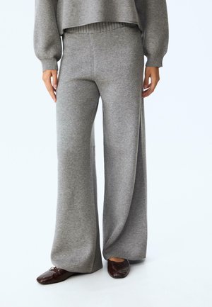 Pantalons gris à jambes larges en tissu tricoté doux avec une ceinture côtelée. Texture lisse, design long, associés à des chaussures marron foncé.
