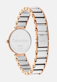Montre en acier inoxydable avec un bracelet à maillons argenté et or rose, un cadran rond et le nom de la marque gravé au dos. Résistante à l'eau jusqu'à 3 bars.