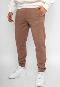 Brune sweatpants med en tætsiddende ben-design, der har sidelommer og et broderet "Dropsize" logo fortil. Blød tekstur og elastiske manchetter.