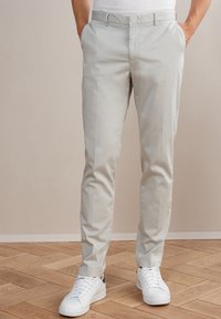 Ljust grå chinos med en jämn textur, med två sidofickor och en rak bendesign, kombinerat med vita sneakers.