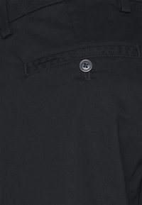 Pantalon en tissu noir présentant une poche arrière avec une fermeture par un seul bouton noir, une texture lisse et une coupe droite.