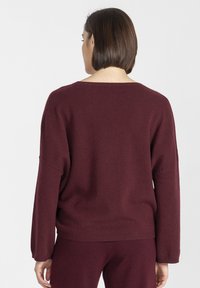 Burgundowy, luźny sweter wykonany z miękkiego materiału, z opuszczonymi ramionami, prążkowanymi mankietami i szerokim dekoltem.