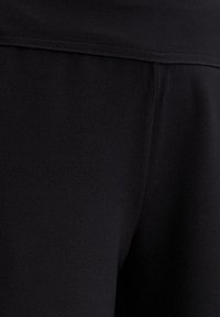Fekete szövet leggings sima textúrával, széles derékpánttal és minimális varrással, a letisztult, áramvonalas megjelenés érdekében.