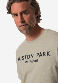 Camiseta de algodón gris claro con el texto "BOSTON PARK" en azul oscuro en la parte frontal y el año de establecimiento 1986, con un clásico escote redondo.