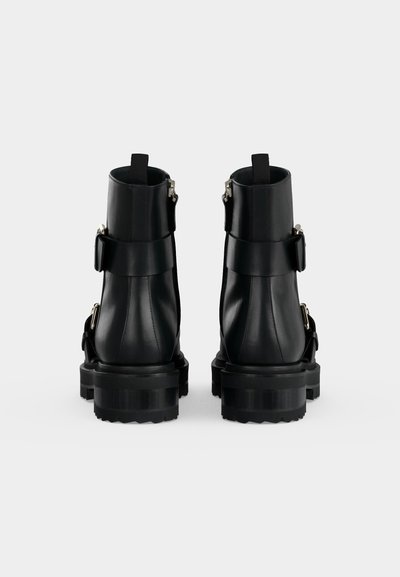 Paire de bottines en cuir noir avec semelles épaisses et boucles, vues de dos sur un fond clair uni.