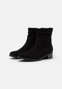 Par de botas de ante negras hasta el tobillo con tacones bajos en bloque y caña ligeramente caída sobre fondo blanco liso.