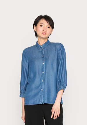 Camisa de ganga com colarinho clássico, frente com botões e mangas longas bufantes. Cor azul média com uma textura suave e um ajuste descontraído.