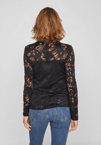Langærmet top i sort blonde med blomstermønster og gennemsigtige ærmer, suppleret af en ensfarvet ryg. Kombineret med blå denim jeans.
