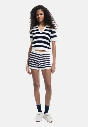 Gebreid top met korte mouwen in marineblauw en wit gestreept, V-hals, gecombineerd met bijpassende gebreide shorts met strepen en een geperforeerd detail. Witte sneakers.