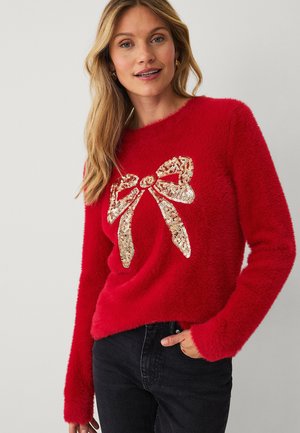 Rød, fluffy sweater med et guldglimtende sløjfedesign på forsiden. Lange ærmer og rund hals. Bæres med mørke jeans. Blød tekstur.