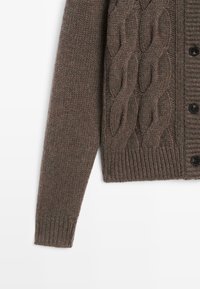 Brune gebreide cardigan met kabelstructuur aan de voorkant, geribbelde manchetten en bijpassende zwarte knopen. Zachte, textuurstof.