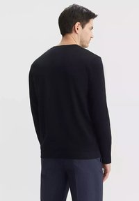 Czarny długi rękaw sweatshirt z okrągłym dekoltem o gładkiej teksturze i prostym wzorze, noszony z spodniami w prążki, ukazując minimalistyczny styl.