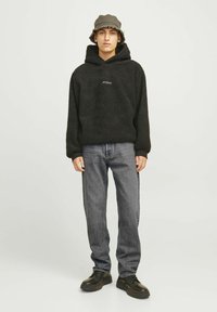 Must must läikehalli fliisist kapuutsiga jakk, millel on kangaroo tasku, kooskõlas hallide teksadega ja mustade jalatsitega. Mudel kannab halli kübarat.