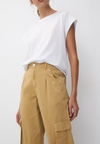 Biała, krótko rękawowa koszulka w połączeniu z khaki spodniami cargo z wysokim stanem, które mają boczne kieszenie i zapięcie na guzik. Gładka struktura.