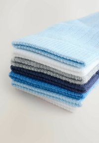 Stapeltje van zeven opgevouwen geribbelde gebreide mutsen in tinten blauw, wit, grijs en marineblauw op een eenvoudige lichte ondergrond.