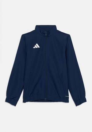 Športna bunda temno modre barve z zadrgo, visokim ovratnikom, dolgimi rokavi, elastičnimi manšetami, dvema sprednjima žepoma in belim logotipom Adidas na prsih.
