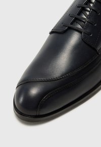 Navy leather shoe with a sleek design, featuring a rounded toe, decorative stitching, and laces at the vamp. Smooth texture with subtle shine.
