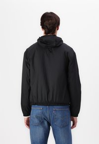 Svart lett hettejakke med elastiske mansjetter og kant, med en teksturert overflate, brukt med blåjeans.