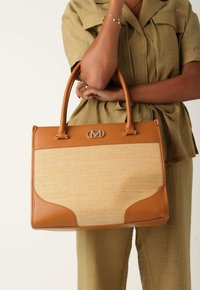 Läderhandväska i tan med flätad mittsektion, styv rektangulär form, handtag upptill och en logotypdetalj. Har både släta och strukturerade ytor.