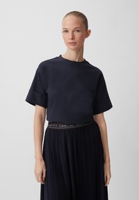 T-shirt in cotone blu navy con maniche corte e colletto rotondo, abbinato a una gonna nera plissettata con cintura elastica marchiata.