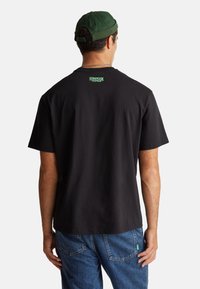 Černé bavlněné tričko s krátkým rukávem. Na zadním límci zelené logo "Stranger Things". Nošeno s modrými džínami.