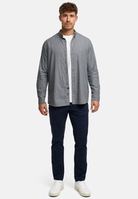 Harmaa nappipaita pitkillä hihoilla, yllä valkoinen t-paita, yhdistetty tummansinisiin housuihin ja valkoisiin lenkkareihin. Sileä kangaspinta.