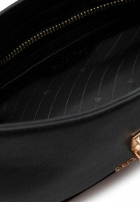 Schwarzes Lederinterieur mit einem goldenen Reißverschluss. Das Futter weist ein dezentes Streifenmuster und Logodetails auf. Eine glatte Textur zieht sich durch das gesamte Design.