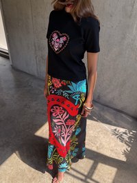 Μαύρη κοντομάνικη μπλούζα με ροζ λουλουδάτη σχέδιο καρδιάς, συνδυασμένη με μια πολύχρωμη φούστα με μοτίβα σε κόκκινο, μπλε και πράσινο λουλουδιών.