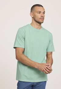 T-shirt en coton vert menthe avec un col rond, des manches courtes et une coupe décontractée, porté avec un jean en denim bleu. Design simple et uni.