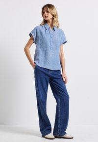 Hellblau gestreiftes Kurzarmhemd mit Kragen und Knopfleiste, kombiniert mit weit geschnittenen Denim-Jeans und lässigen weißen Sneakern.