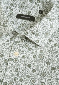 Blommönstrad bomullsskjorta med vit bakgrund, med gröna och bruna blommor. Inkluderar en klassisk krage och en krämfärgad knapp.