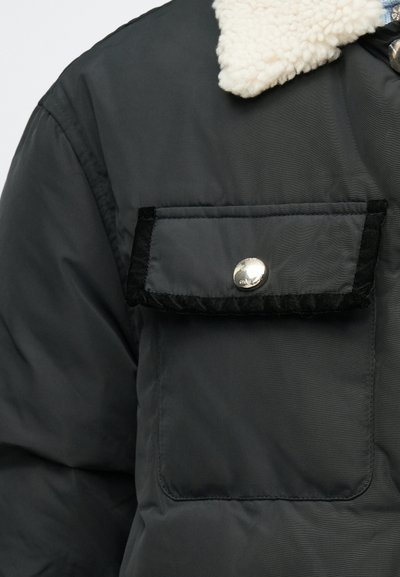 Sort polstret jakke med en cremefarvet faux shearling krave, der har en stor forbavsning lomme med sort velourkant og en sølvfarvet trykknap.