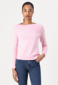 Lys rosa genser med lange ermer, rund hals og ribbede mansjetter. Liten logodetalj på brystet. Stoffet ser glatt og mykt ut.