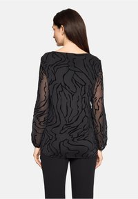 Czarna bluzka z długim rękawem i przezroczystymi rękawami, ozdobiona teksturowanym abstrakcyjnym wzorem oraz subtelnym warstwowym designem, widok od tyłu.