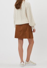 Crème kabelgebreide trui met ballonmouwen, gecombineerd met een bruine suède rok en witte sneakers met beige accenten. Eenvoudig ontwerp, casual uitstraling.