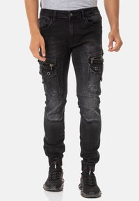Pantalons cargo en denim noir avec plusieurs poches zippées et à rabat, bas effilés, emplacements décolorés et sections de genoux renforcées.
