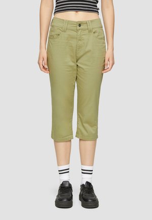 Khaki skrátené nohavice so slim fit strihom, so zapínaním na gombík, pútkami na opasok a prednými vreckami. Kombinované s čiernymi teniskami a bielymi pruhovanými ponožkami.